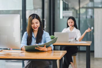 Fototapeta premium Smiling call center agents wearing headsets, working at desks with computers and documents in a modern office.