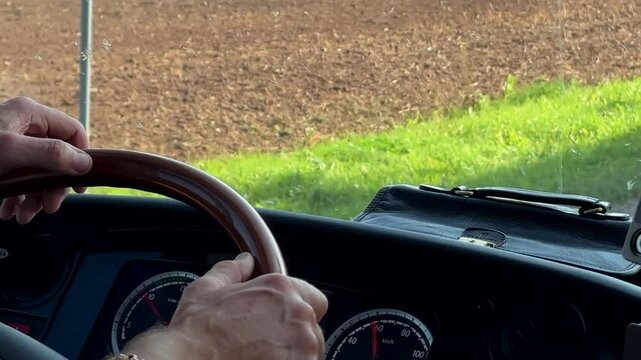 Bus or coach driver's hands on steering wheel driving on road in Lithuanian countryside.