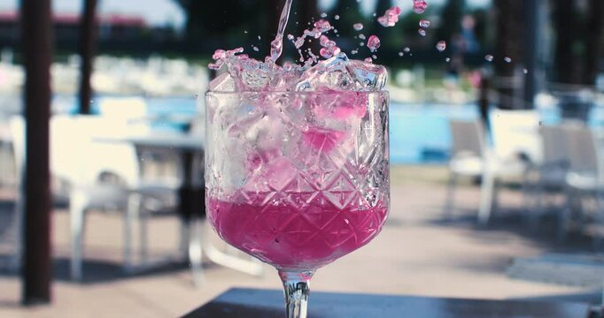 Super slow motion close up of bartender is preparing alcoholic cocktail in transparent glass for customer at poolside bar of luxury hotel resort during summer holidays vacation at 1000 fps.