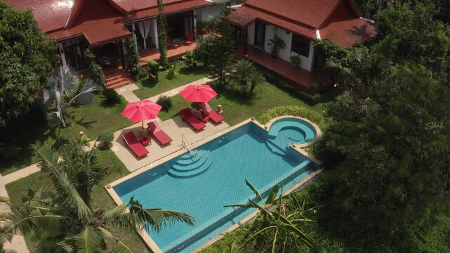 A beautiful aerial view of a tropical villa with red roofs, a swimming pool, and lush gardens