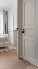 A slightly open door reveals a bedroom with a white bed and a grey and white bedspread. The room is lit by natural light