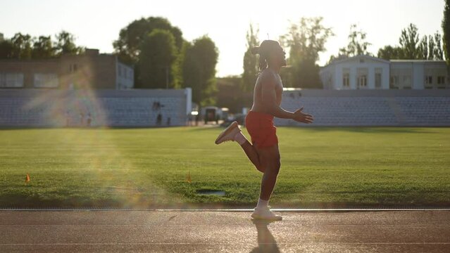 A male sprinter in red men's athletic shorts quickly running a stadium running track past the camera on a sunny autumn day