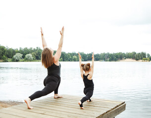 family workout - mother and daughter doing exercises on beach. Mom and child working out on lakeside in the morning.