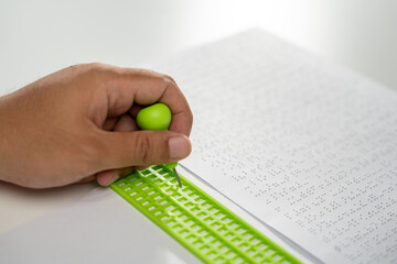 Close up Hand of a blind person writing some braille text on page paper. Young blind man using slate and stylus tools making embossed printing the braille alphabet Code on sheet.