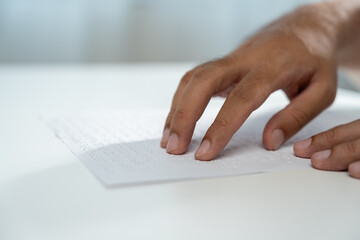 Hand of a blind person reading some braille text on page paper to learn. Finger of blind student...