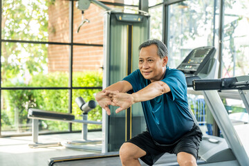 Senior asian man wearing sportswear warming up in fitness gym before exercise. Mature man stretching arm before running. Training athlete work out