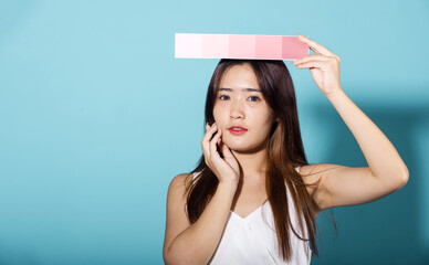 Portrait of happy female hold color card under sun protection studio shot isolated on blue background, Asian beautiful young woman smiling and holding skin color scale paper, skincare beauty face