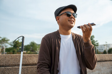 Young asian blind man using application on mobile phone to helping accessibility for persons with...