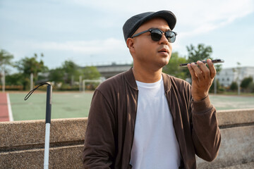 Young asian blind man using application on mobile phone to helping accessibility for persons with...