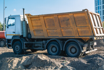 Obraz premium A dump truck at a construction site. Transportation of bulk building materials for use in construction. Self-unloading dump truck. Delivery of construction materials to the construction site.