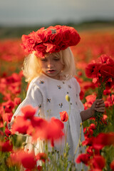 A young girl wearing a red flower crown stands in a field of red poppies. The scene is serene and peaceful, with the girl being the focal point of the image.