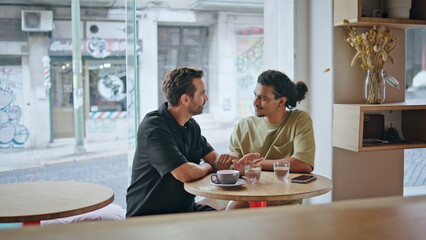 Carefree gay partners talking at romantic date in coffee house. Lgbtq couple 