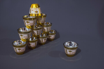 A set of golden oriental teacups arranged like a pyramid, on a gray background.  © Sefianto Studios