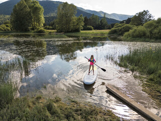 Girl child stand-up paddleboarding on a calm lake, aerial shot. Sup board, sport, and recreation concepts.