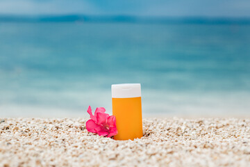 Bright sunscreen bottle on pebble beach with sea as background. Concept of minimalist design of advertisement of sunscreen or cosmetics. Protection against ultraviolet rays or harmful effects of sun