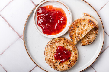 Hot Toasted Crumpets with piece of butter on a plate with strawberry jam. Perfect tasty breakfast popular in England, UK