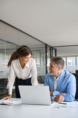 Vertical photo of professional mature business man and woman colleagues having conversation at work. Two happy professional executives company team working in corporate office using pc laptop computer