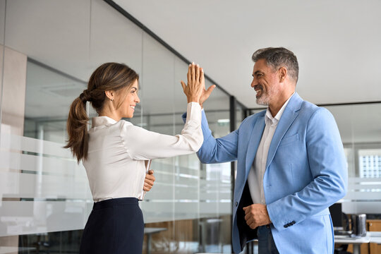 Two happy cheerful professional business team people executives middle aged man and woman giving high five in office celebrating corporate success, teamwork achievement and leadership at work.