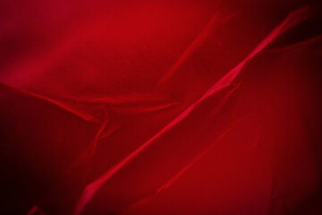 Extreme close up of red empty plastic bag background. The plastic surface is wrinkly and tattered making abstract pattern. Selective focus, shallow depth of field.