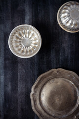 Vintage pewter plate and bowls on black chalkboard background. Flat lay. Top view. Food concept. Dark mood food photography.