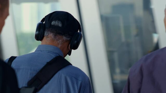 Passenger with headset stand by the tracks waiting for the train that finally comes past them at the station during rush hour..