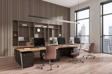 Coworking interior with armchairs and desks, pc monitors and shelf near window