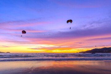 Silhouette of parasailing and people on the beach with the Most beautiful and colourful sunset on Patong Beach Phuket Island Thailand