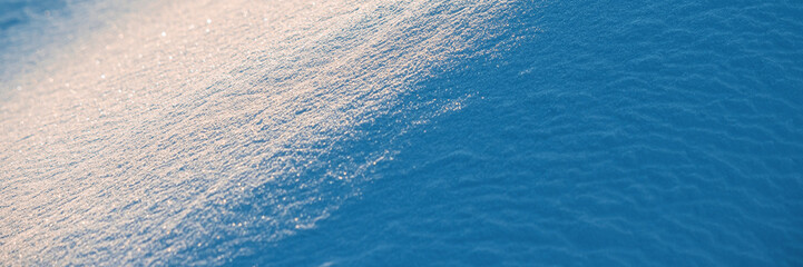 Obraz premium Beautiful winter background with snowy ground. Natural snow texture. Wind sculpted patterns on snow surface. Wide panoramic texture for background and design. Closeup top view with copy space.