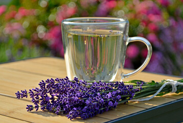 napój w szklance na stole obok bukietu lawendy, napój z lawendą w przeźroczystej szklance, herbata ziołowa z lawendą na stole obok kwiatów lawendy, stolik bambusowy, herbal tea with lavender