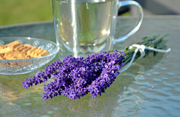 napój z lawendy w szkalnce na stoliku ogrodowym, lawenda na stole obok szklnki,lavender drink in glass and lavender flowers, drink with lavender and lavender flowers on glass coffee table © kateej