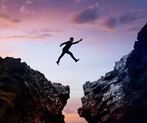 A person jumping between two cliffs against a sunset sky, symbolizing challenge and risk. Generative AI