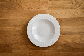 Ceramic white flat plate for food on wooden table top view
