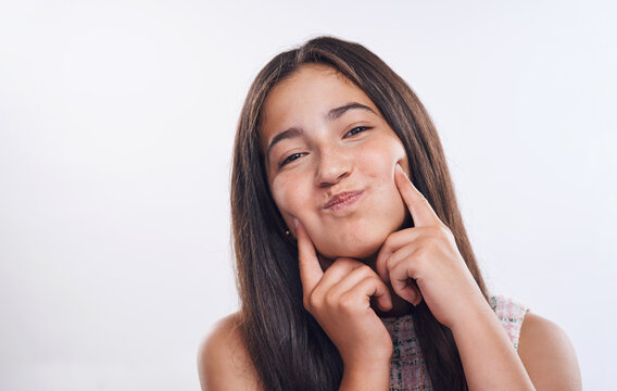 Girl, teenager and funny face with cheeks in studio portrait for joke, happy and fingers by white background. Person, model and smile with hands, dimples or comic emoji for humor with mockup space