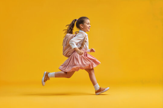 Happy school girl running with backpack on yellow background