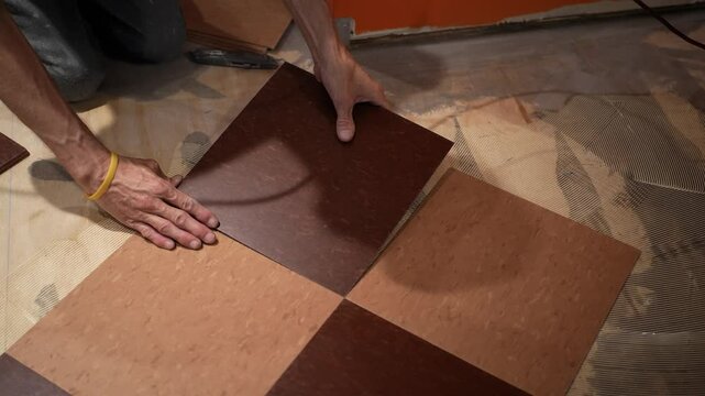 Camera pushes in on two hands putting a vinyl composition tile, VCT into place, pressing it down into the glue for a home renovation project.