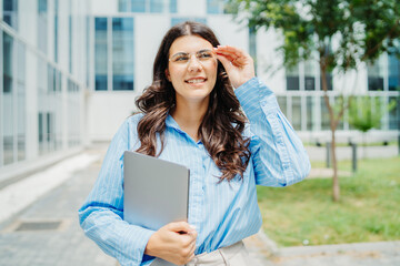 Fototapeta premium One beautiful young successful business woman going to work at business office modern building while holding laptop and waring glasses