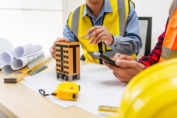 Two men, including a male Asian construction contractor engineer, discuss structural plans and...