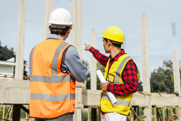 Two male construction workers, including an Asian engineer, meticulously review structural plans...