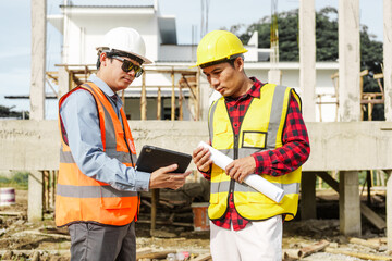 Two male construction workers, including an Asian engineer, meticulously review structural plans...