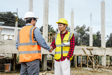 Two male construction workers, including an Asian engineer, meticulously review structural plans...