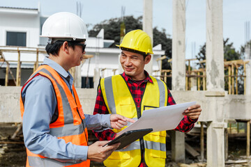 Two male construction workers, including an Asian engineer, meticulously review structural plans and design concrete columns and beams for a new residential build.