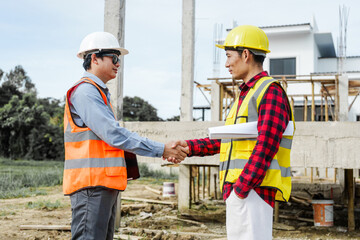 Two male construction workers, including an Asian engineer, meticulously review structural plans...