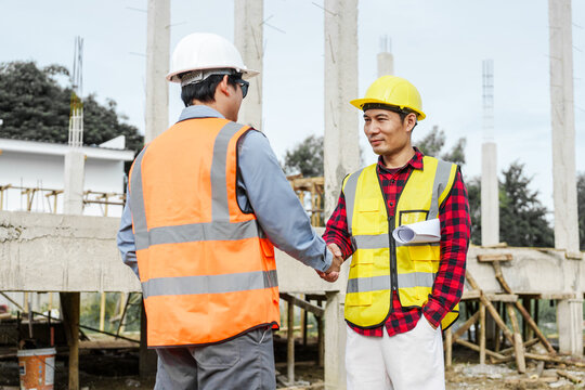 Two male construction workers, including an Asian engineer, meticulously review structural plans and design concrete columns and beams for a new residential build.