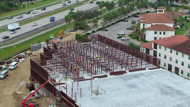 Construction works on metal walls of commercial building. Blue collar workers at large site with scattered equipment. Development of residential housing in America
