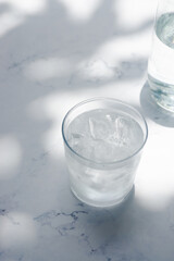 a glass of cold water with ice on marble table in the morning sunlight.