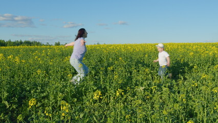 Fototapeta premium Young Mother With Son Enjoy Playing With His Mom In Yellow Rapeseed Field Countryside. Happy Little Boy With Hat. Countryside.