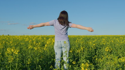 Woman Standing In Yellow Rapeseed Field Raising Her Arms Expressing Freedom. Beautiful Healthy Caucasian White Woman Standing In Blooming Rapeseed Field And Looking At Horizon.