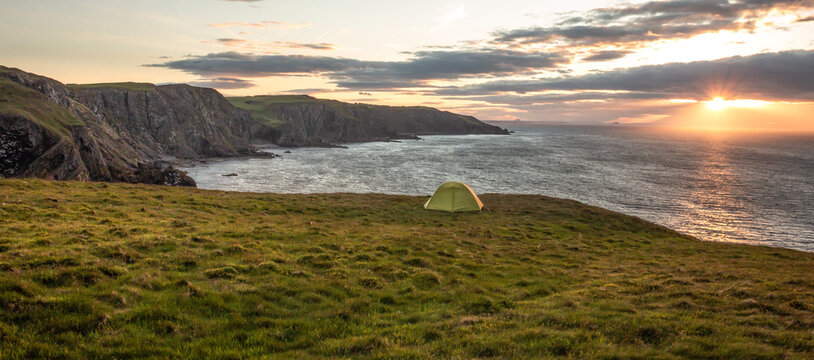 Green camping tent on a grassy cliff at sunset at St. Abbs Head, east coast of Scotland