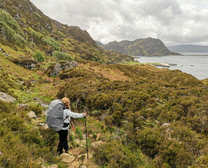 Naklejka premium Woman with hiking poles and hiking backpack looking at coastal landscape in west coast of Scotland