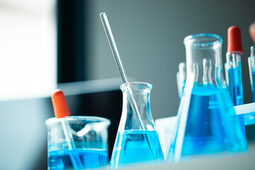 A row of blue beakers with a blue liquid in them. The beakers are arranged in a row and are all the same size
